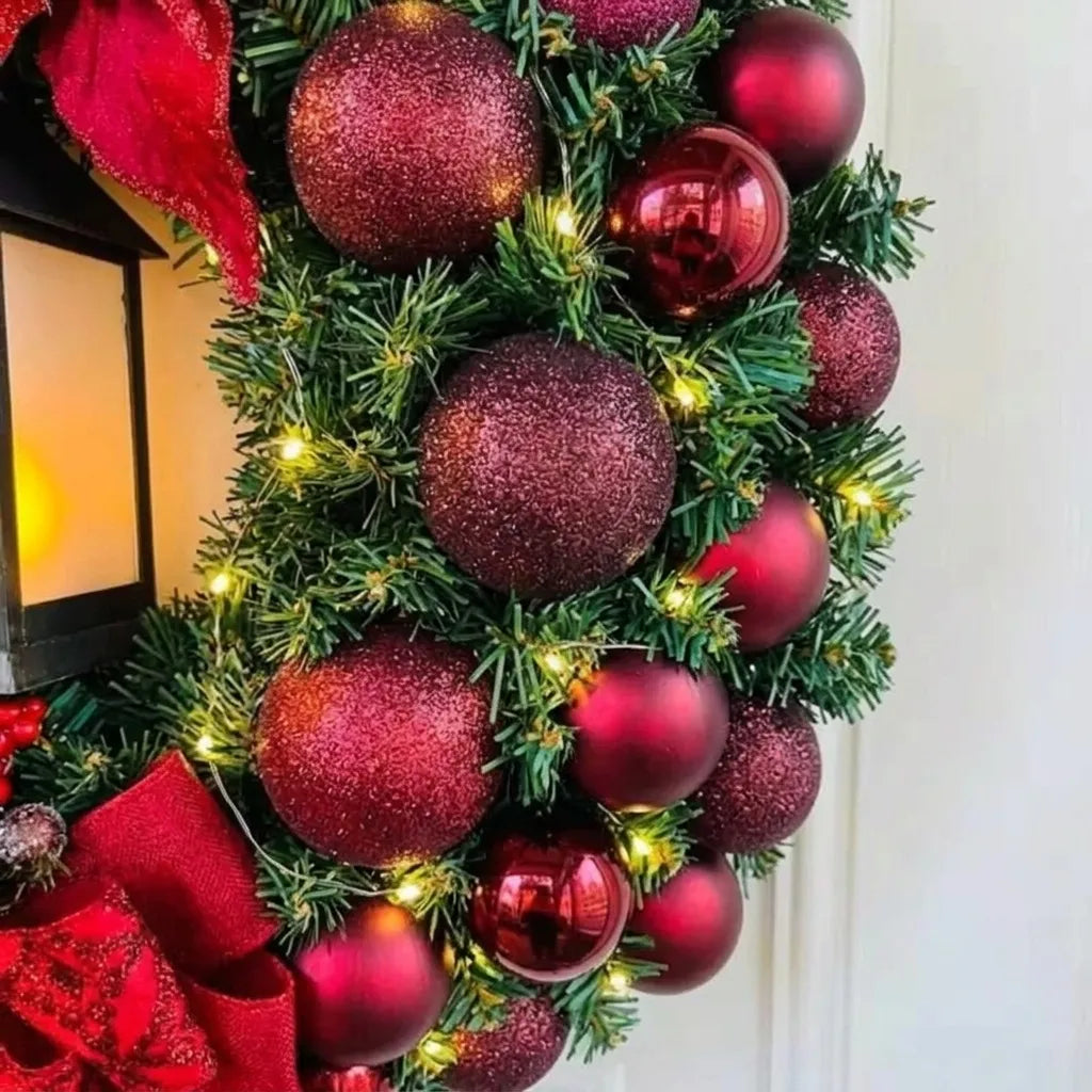 Detalhe das bolas vermelhas e vinho, folhagem verde e pontos de luz da guirlanda de Natal com lanterna de 30 cm