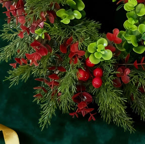 Detalhe das folhas verdes, ramos e bagas vermelhas da guirlanda de eucalipto de 40 cm.