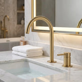 Torneira Salerno para banheiro ouro escovado, instalada em bancada de mármore branco com espelho de LED — Toque de Casa