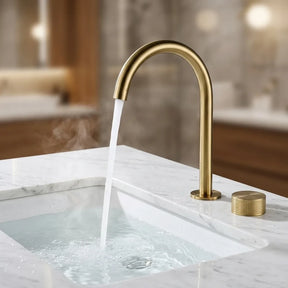 Torneira misturador dourado escovado com água corrente em cuba de embutir sobre bancada de mármore branco, close em ângulo de 45°