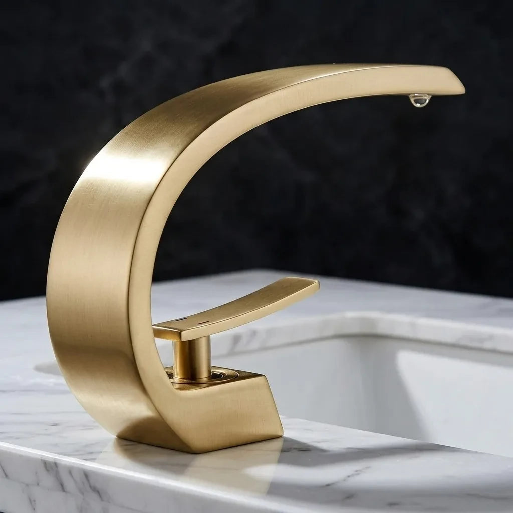 Torneira para banheiro monocomando luxury dourada escovada quente e fria, vista em ângulo 45° destacando o design curvo — Toque de Casa